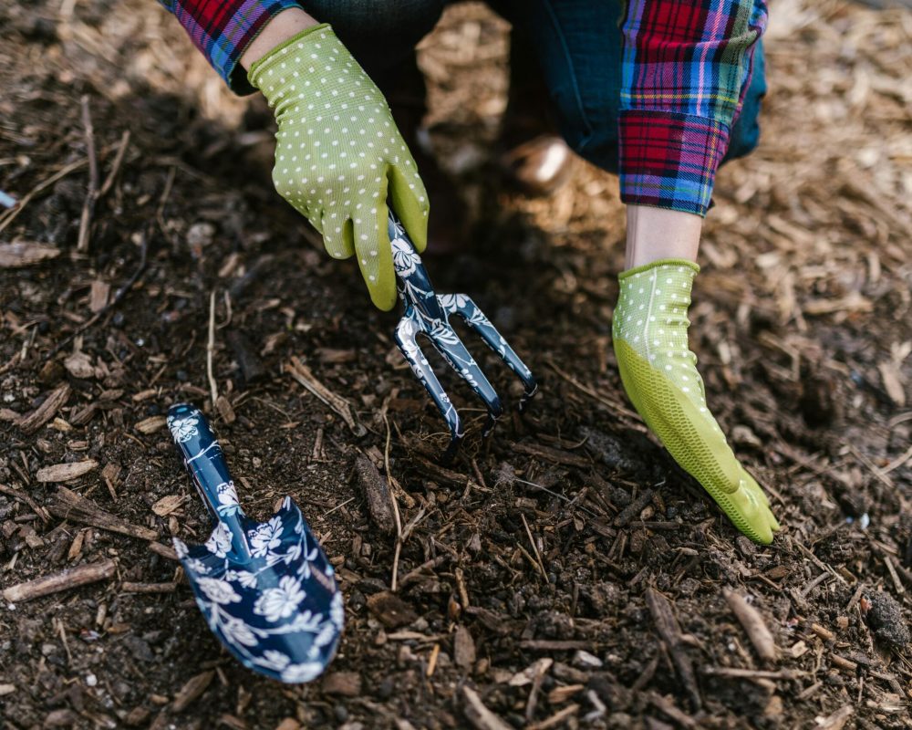 A person wearing gloves using garden tools in soil for planting.